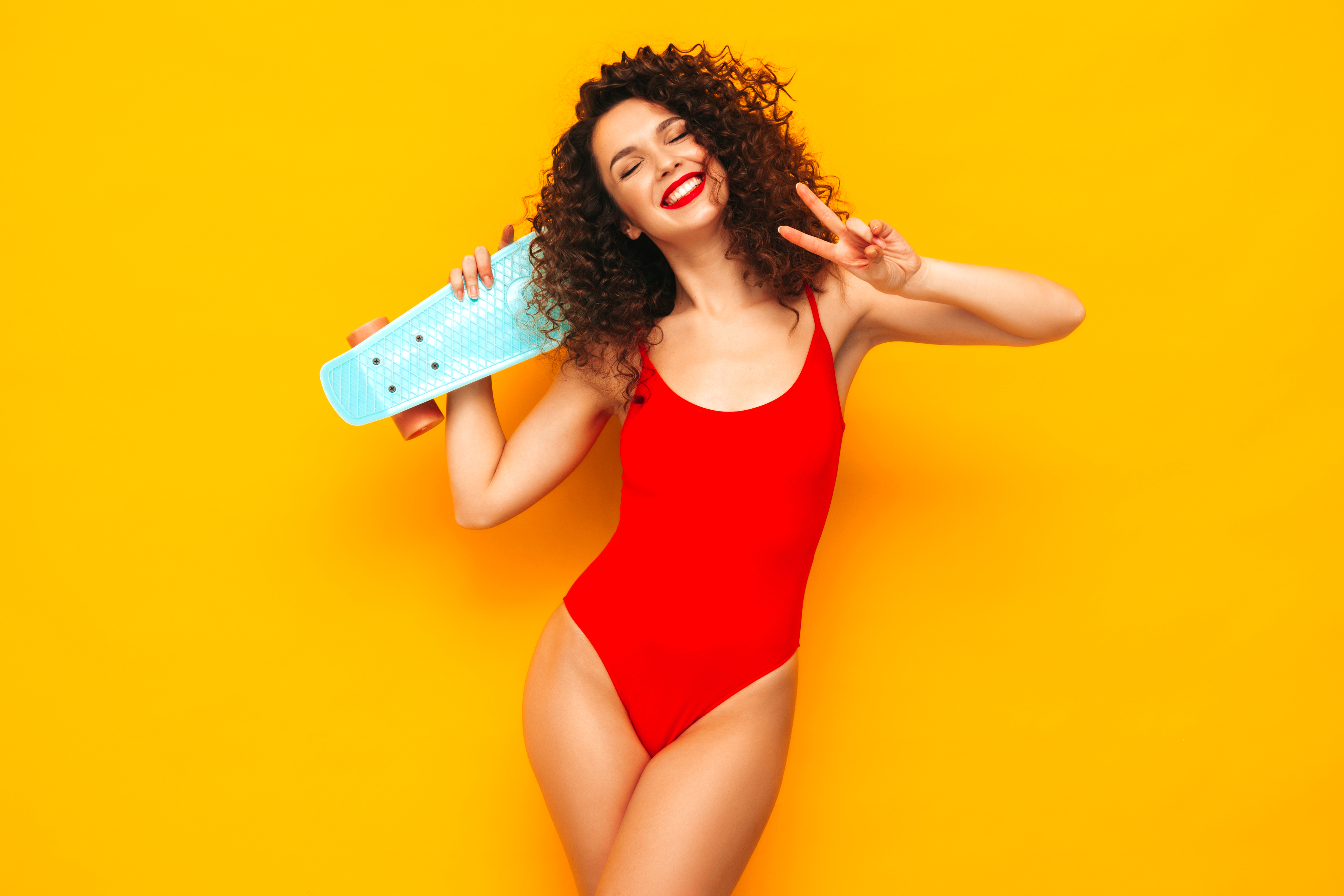 young beautiful sexy smiling woman posing near yellow wall studiotrendy model red summer swimwear bathing suitpositive female with afro curls happy cheerful holding penny skateboard Хубави неща - магазин за подаръци | hubavineshta.bg